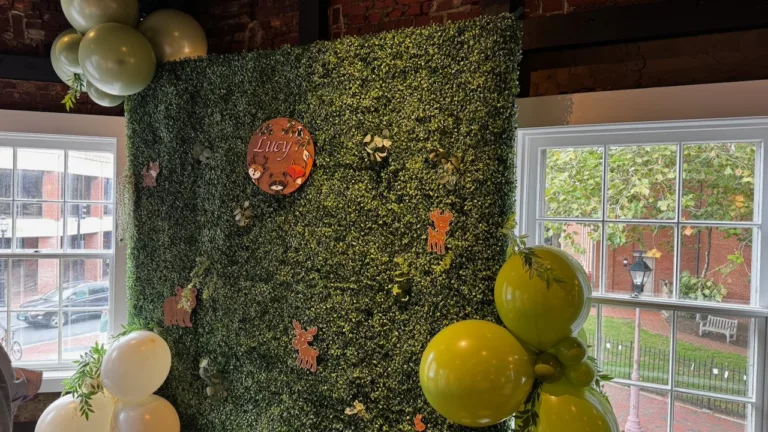 Greenery hedge photo backdrop with woodland animal cutouts, a 'Lucy' name sign and green and white balloons, baby shower decor in Annapolis, MD