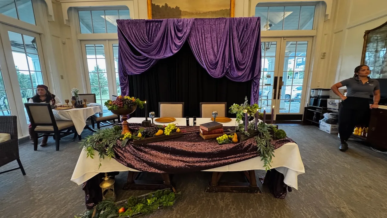Head table with purple draped fabric backdrop, sequined runner, greenery garland, fruit and candle centerpieces, Harry Potter themed 60th birthday party decor in Dumfries, VA