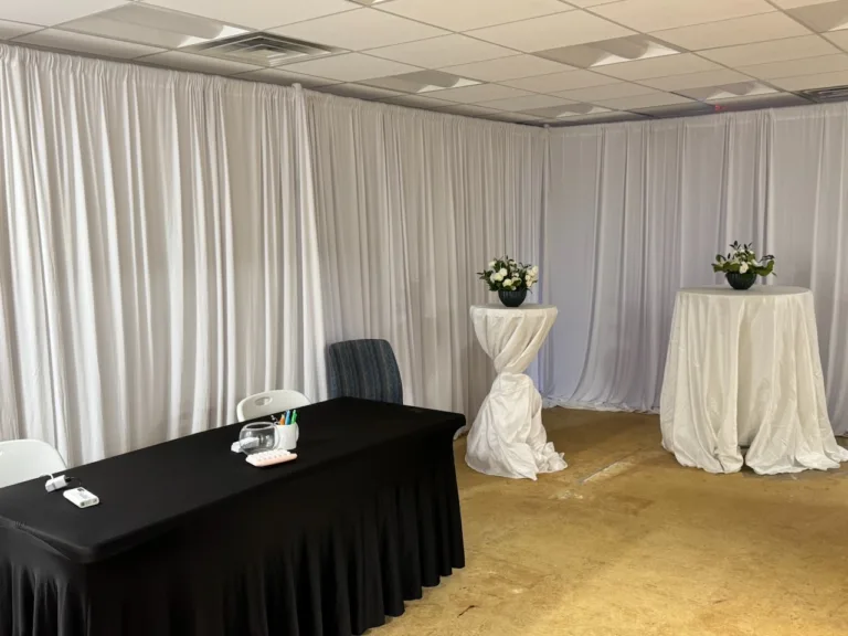 White drapery room with black-draped table and white cocktail tables with floral centerpieces at the Jae Kim grand opening in Fairfax, VA