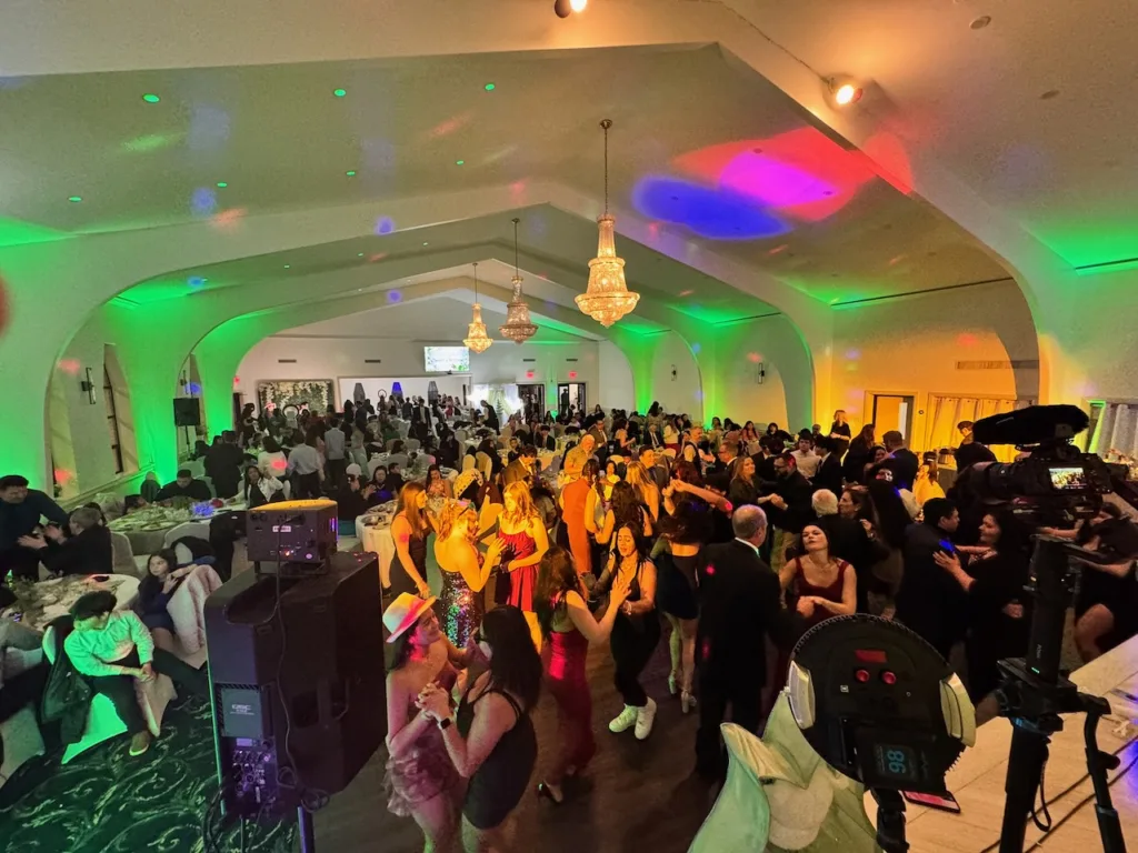 Large crowd celebrating with colorful uplighting and chandeliers at Jimena's quinceañera in Silver Spring, MD