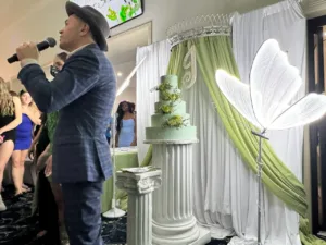 Emcee speaking into microphone beside the light green quinceañera cake with butterfly decor at Jimena's quinceañera in Silver Spring, MD
