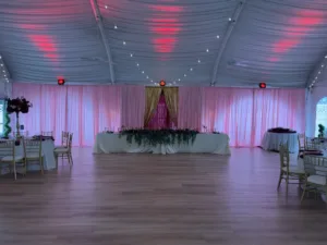 Tented reception hall with draped ceiling, pink uplighting and sheer curtains, head table with greenery and burgundy florals and gold chiavari chairs, quinceañera decor in Columbia, MD